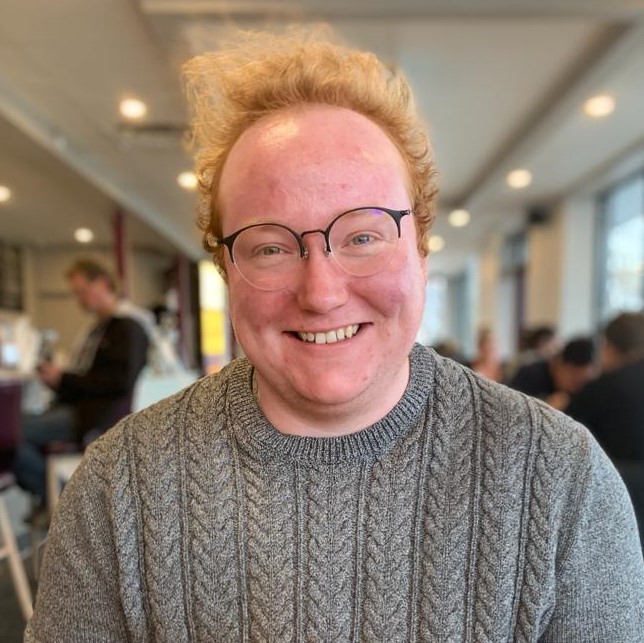 Caleb, a white man with curly red hair and large round glasses smiling.